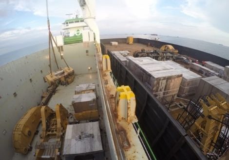 Crane lifting heavy mining machinery onto boat for transportation