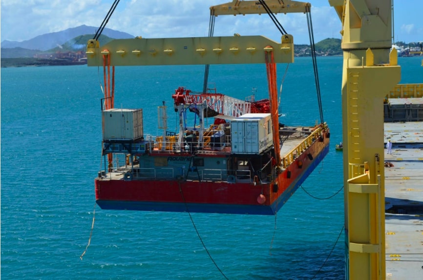 Crane loading mining machines from landing craft to vessel