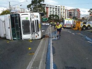 Workers tending to a crashed white truck lying on its side on the road