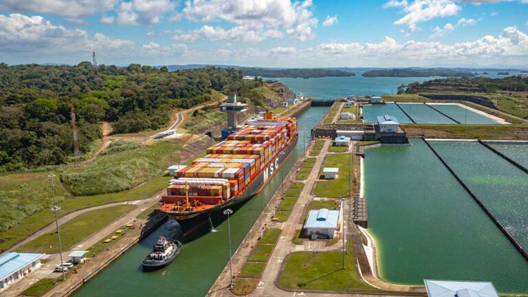 Large, full containership is guided into a panama canal lock by a tugboat