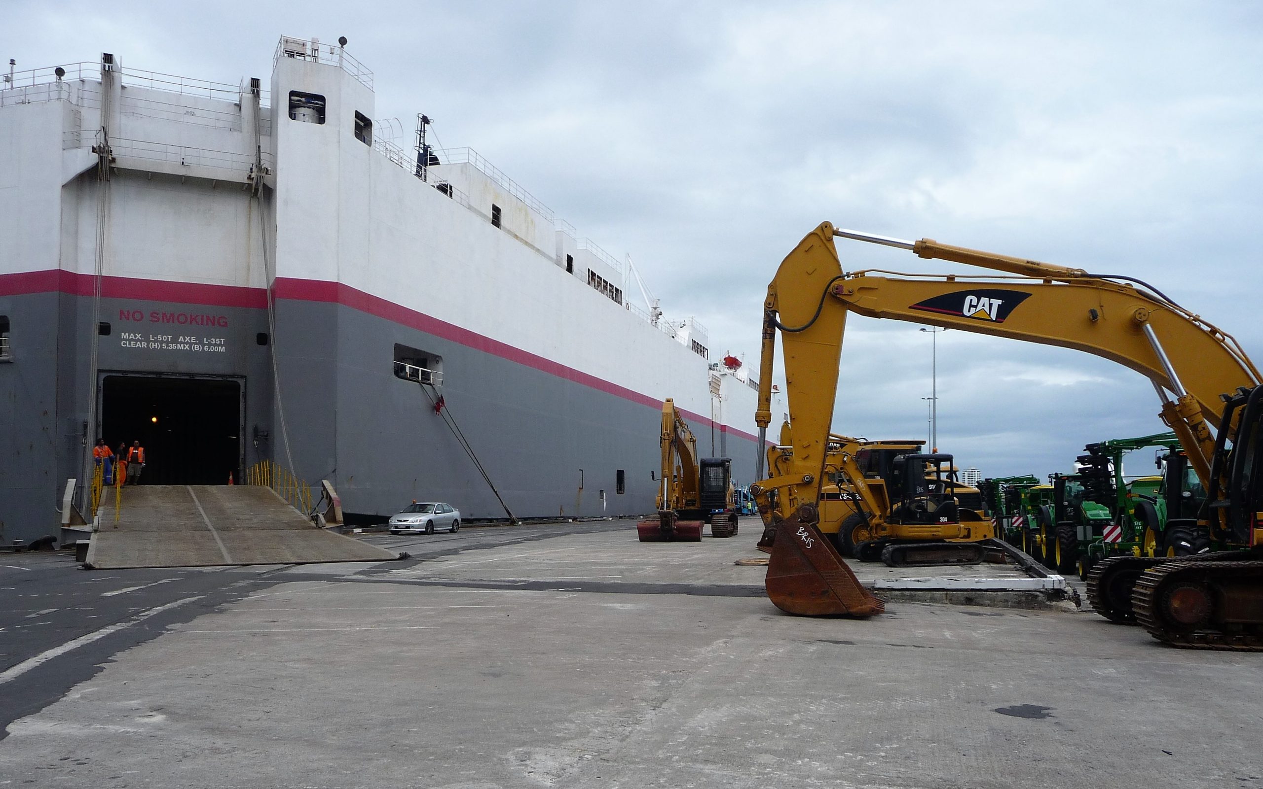 Caterpillar excavators line the right of the image, waiting to be loaded unto large RORO vessel picture in the left of the frame