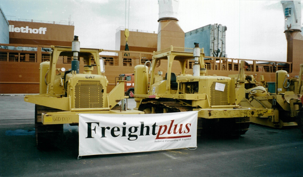 Two CAT brand pipelayers at port with "freightplus' logo banner hanging between them
